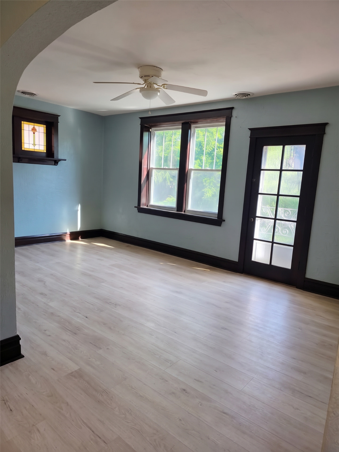 Completed whitewashed vinyl plank flooring in a bright room with dark wood trim and a stained glass window