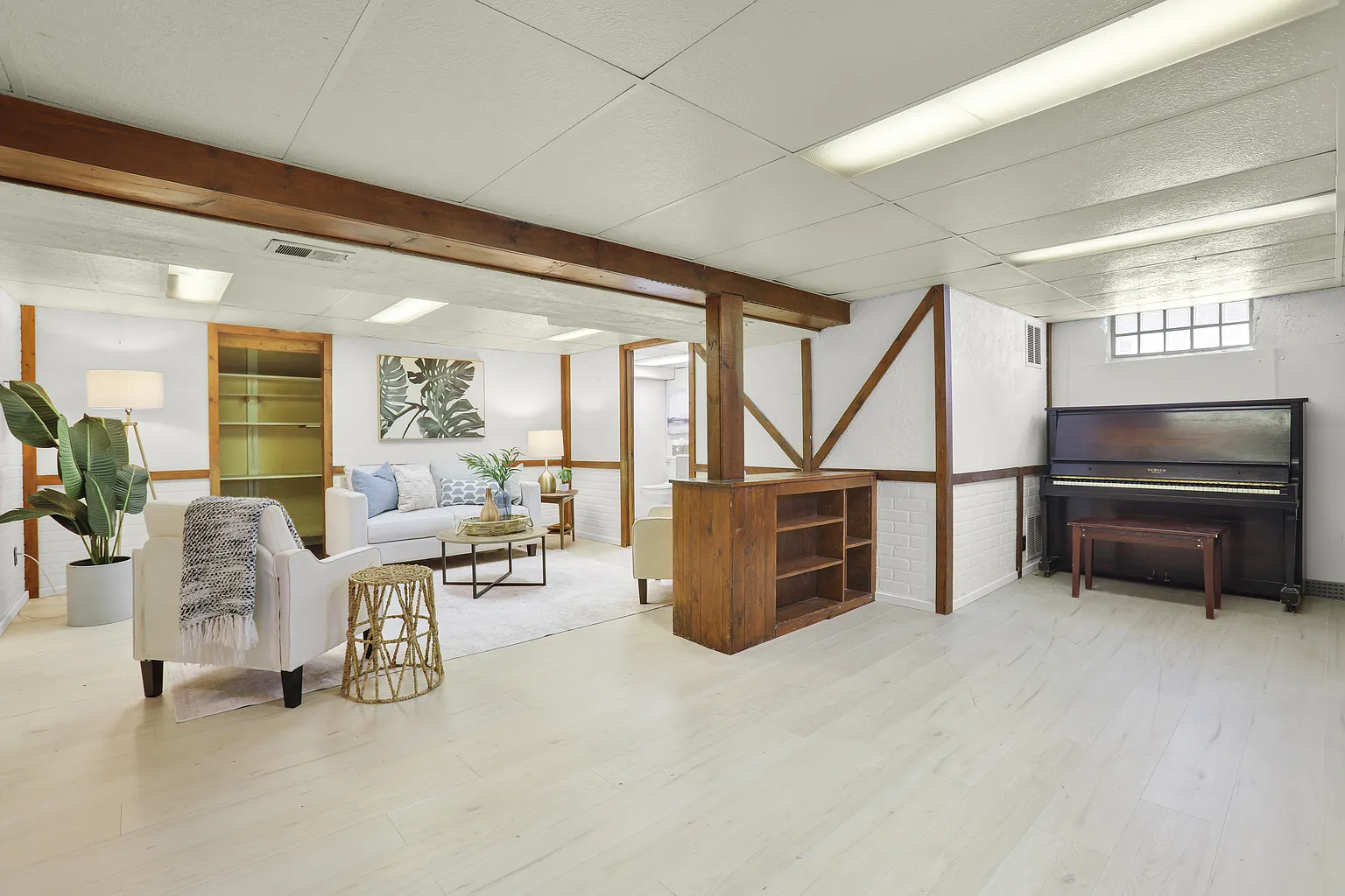 Completed light vinyl plank flooring in a finished basement living area with wood beams and white brick walls