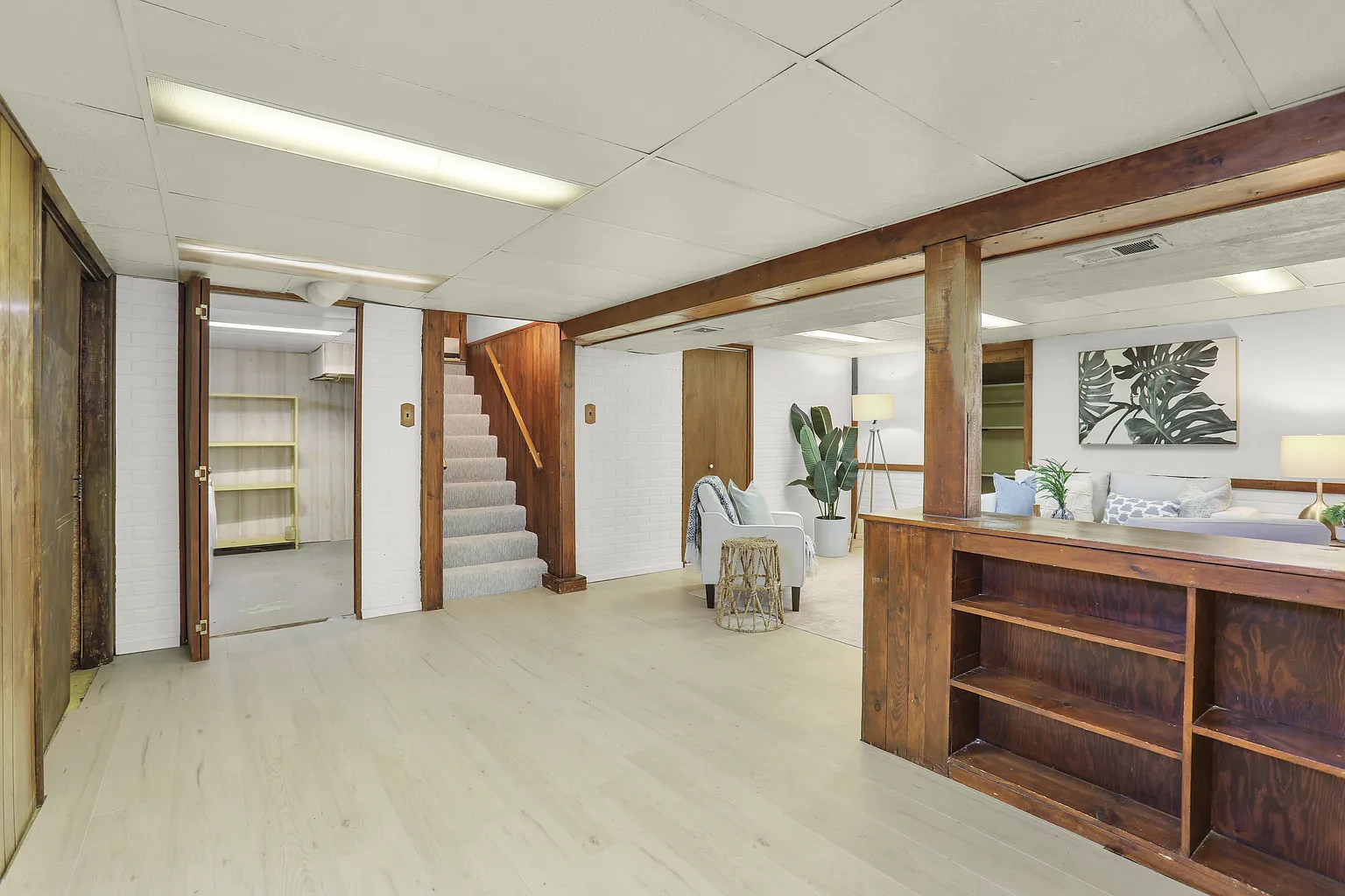 Completed light vinyl plank flooring in a finished basement with wood shelving and staircase